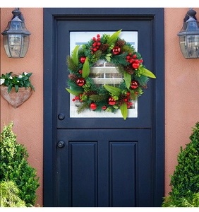Christmas wreath with red berries and pine cones hanging on a dark blue front door