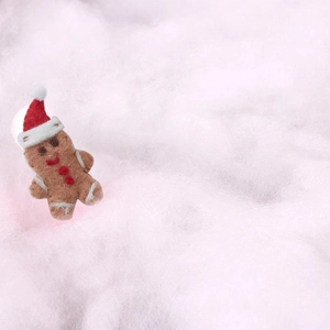 Brown felt gingerbread man doll with red hat on pink snowy cotton holiday background