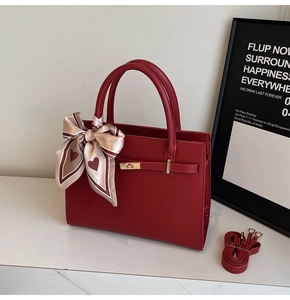 Detail view of red commuter handbag featuring gold metal turn-lock and elegant silk scarf
