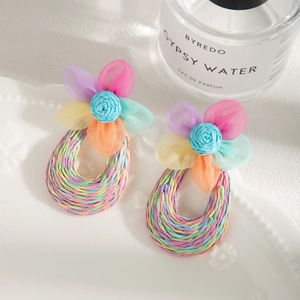 Handmade raffia woven floral earrings with blue rose and mesh petals on ceramic dish