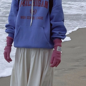 Foto de guantes de lana táctiles rosas usados con sudadera azul en la playa