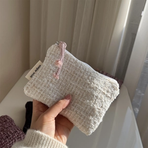 Close-up of off-white tweed pouch with woven texture and a pink rope zipper puller