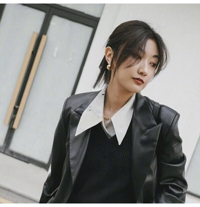 Close-up of golden spherical stud earrings worn by a model with a black leather blazer