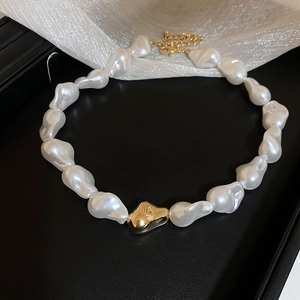 Gros plan d'un collier de perles baroques avec pendentif doré sur plateau à bijoux