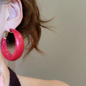 Close-up of a large red leather C-shaped hoop earring worn by a model in profile