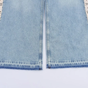 Close-up of light blue denim hem featuring white lace stitching and frayed edge details