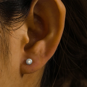Macro shot of silver stud earring with white opal and cubic zirconia on model's ear