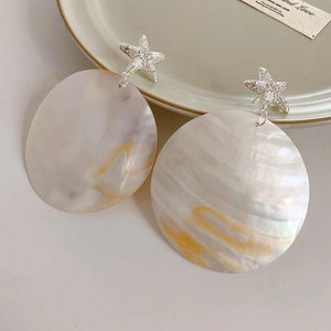 Macro shot of seashell circle earrings with silver starfish detail on a ceramic tray