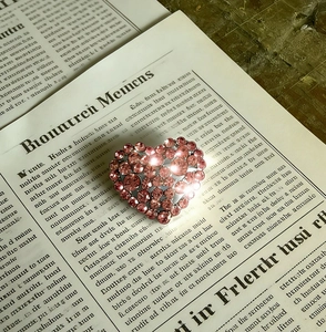 Macro shot of a pink rhinestone heart brooch on a vintage newspaper background