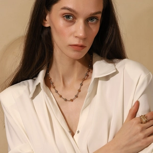 Close-up of model wearing two-tone beaded necklace and vintage gold oval gemstone ring