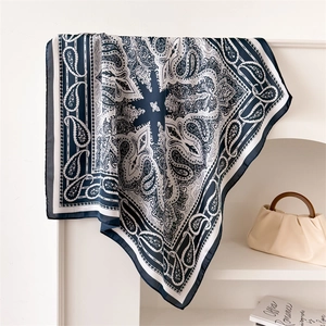 Navy blue and white paisley silk-like square scarf draped on a rack with a handbag