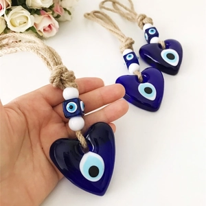 Trois pendentifs cœur œil porte-bonheur en verre bleu avec corde de jute tenus à la main