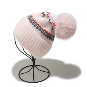 Details einer rosa Strickmütze mit großem Pelzbommel und geometrischem Wellenmuster