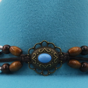 Detailed close-up of a blue felt hat featuring a bronze medallion and wooden beads