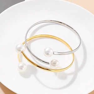 Minimalist open pearl bracelets in gold and silver finish on a white ceramic plate