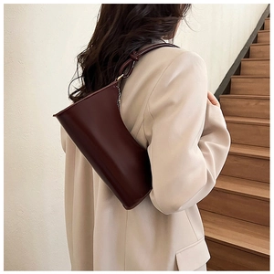 Macro shot of dark red leather baguette bag with knotted shoulder strap detail on a model