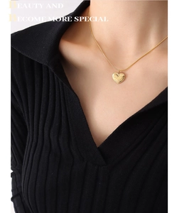 Close-up of engraved gold heart pendant on a snake chain worn with a black V-neck top