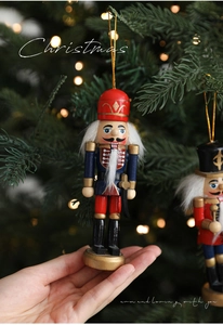 Handgehaltener 13cm Nussknacker-Soldat aus Holz vor einem geschmückten Weihnachtsbaum