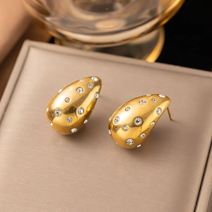 Golden teardrop earrings with white zircon on champagne leather display stand