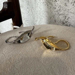 Detail of gold and silver leaf-shaped rings with metallic texture on beige fabric