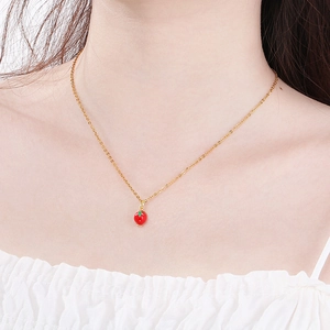 Close-up of a cherry pendant necklace on a gold chain worn on a woman's neck
