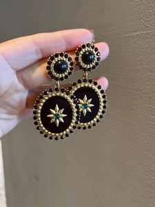 Detail of vintage matte gold starburst earrings with black resin and green crystal