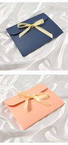 Detail of navy and pink envelope gift boxes with silk bows on white satin background