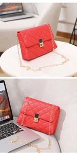 Detail of red quilted shoulder bag with gold chain strap and metal lock on a white table