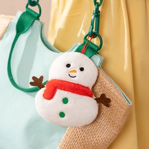 Close-up of a white plush snowman charm with red scarf and green buttons on a woven bag