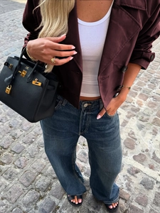Detail einer weinroten Jacke mit Knöpfen, kombiniert mit weißem Top und Jeans