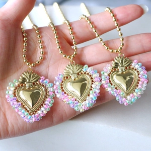 Detail of three golden ball chain necklaces with colorful beaded heart pendants in hand