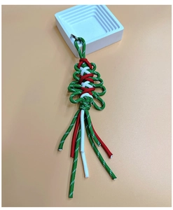 Macro shot of handmade woven green Christmas tree keychain with red and white rope detail