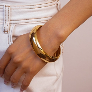 Detail of a minimalist wide golden cuff bracelet with a polished metallic finish on wrist