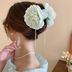 Detail of a green fabric flower hair claw with dangling rhinestone tassels on wavy hair