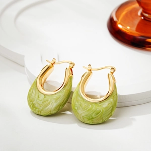 Close-up of gold U-shaped earrings with light green marble enamel on a minimalist tray