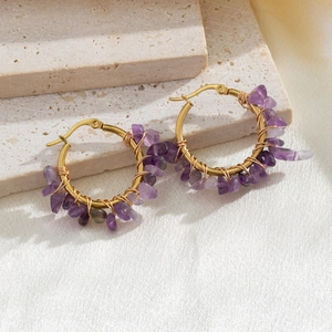 Handmade gold hoop earrings with purple natural stones on a white stone background