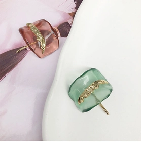 Detailed close-up of pink and green resin earrings with elegant gold accents on a white plate