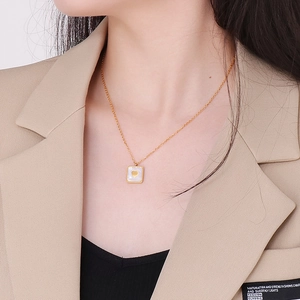 Detail van gouden vierkante ketting met witte schelp en hart gedragen op de halslijn