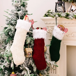 Three premium knitted Christmas stockings in white, red and green hung by a cozy fireplace