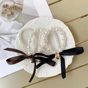 Detail of elegant pearl bracelet with silk bows and gold heart charms in a white dish