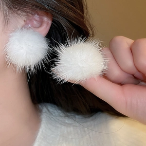 Detail view of a white fuzzy faux fur pom pom earring worn by a model in close-up shot