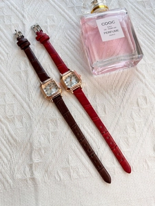Elegant rose gold square watches with dark brown and red leather straps on soft fabric