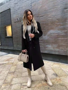 Full-length street style shot of a black double-breasted wool coat with notch lapels