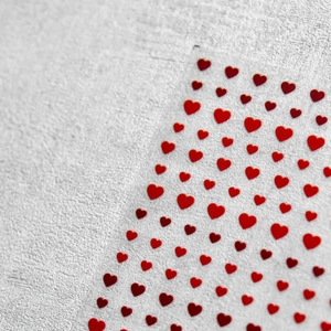 Macro detail of red heart nail art stickers on a transparent sheet over a stone surface