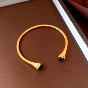 Macro shot of vintage gold bangle featuring green stones and zircon accents on a stand