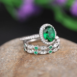 Macro detail of oval emerald halo ring set with wavy diamond bands on a dark rock