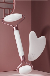 Close-up of white marble facial roller and heart guasha tool with rose gold metal accents