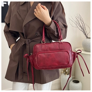 Detail of dark red faux leather handbag featuring side bow ties and double handles