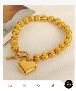 Detail shot of golden beaded heart bracelet with toggle clasp on beige fabric texture