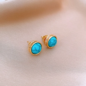 Gold plated turquoise stud earrings with zircon halo on orange silk background